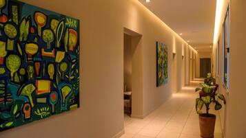 A hallway with artwork on the walls, a potted plant, and a door at the end.