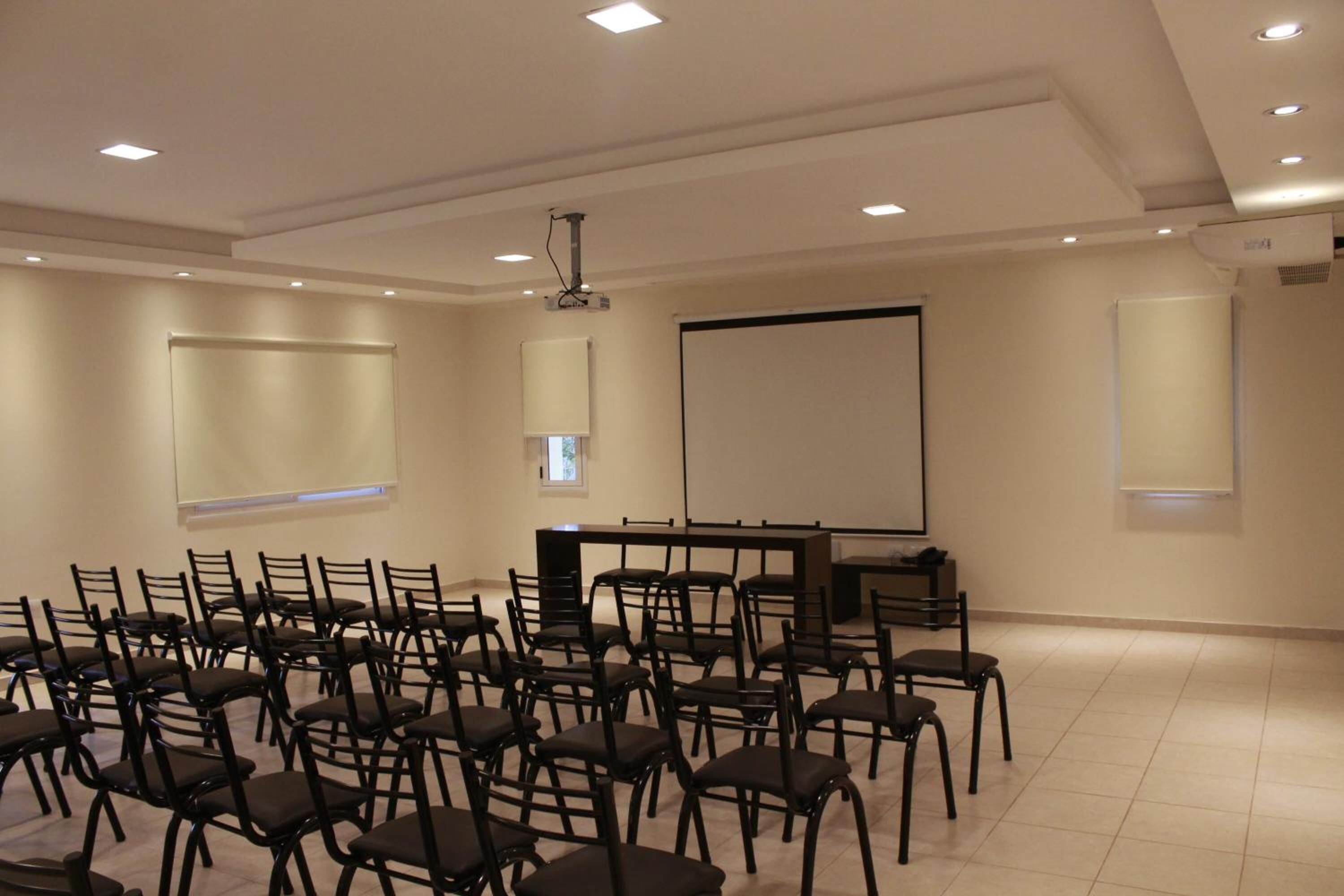 A conference room with rows of chairs, a projector, and a screen.