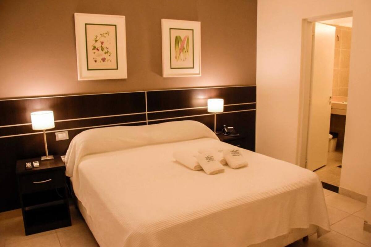 Una habitación de hotel con una cama grande, dos mesitas de noche y lámparas de pared.