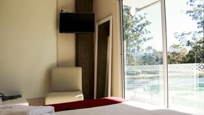 Une chambre d’hôtel avec un lit, une chaise, une télévision et une vue sur une piscine extérieure.