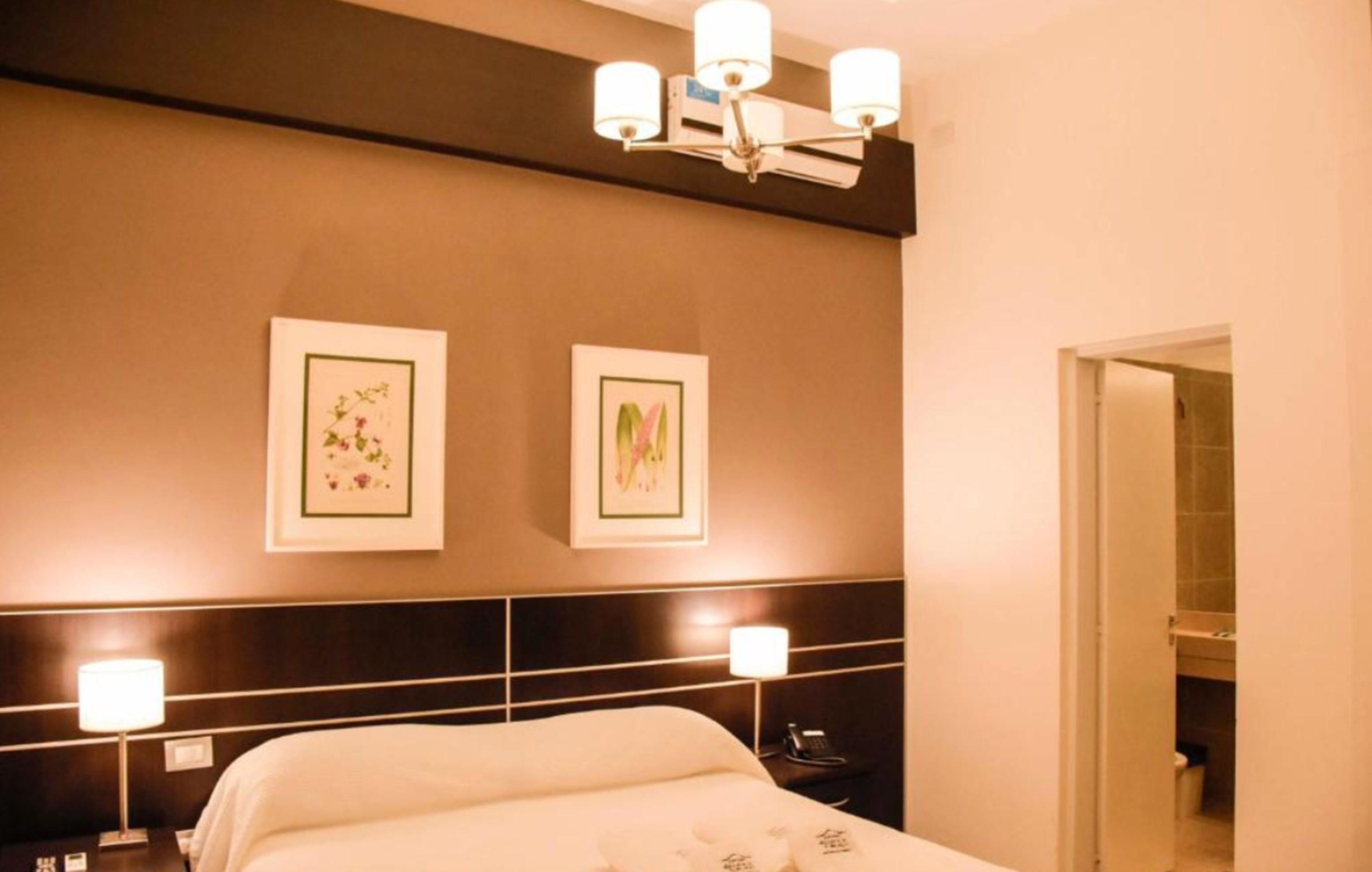 A hotel room with a bed, bedside lamps, a wall-mounted air conditioner, and framed artwork.