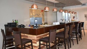 Un espace bar moderne avec un comptoir en bois, de nombreuses suspensions en cuivre et plusieurs chaises de couleur marron foncé.