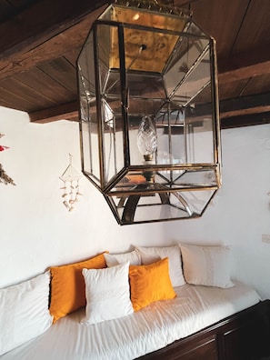 Une pièce avec un plafond en bois, un lustre en verre et un canapé blanc agrémenté de coussins orange.
