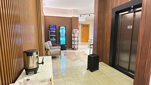 Eine Hotellobby mit Empfangstresen, Getränkeautomaten, einer Kaffeemaschine, einer Sitzecke und einem Aufzug.