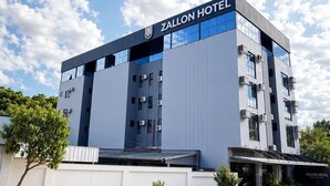 Ein modernes Zallon Hotel Gebäude mit flachem Dach, großen Fenstern und einer Beschilderung auf der Spitze.