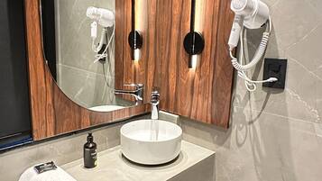 A modern bathroom with a round sink, wooden vanity, a large mirror, and two hair dryers mounted on the wall.