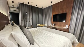 Ein modernes Hotelzimmer mit einem großen Bett, einem Schreibtisch mit Flachbildfernseher und einer Sitzecke mit Tisch und Stühlen.