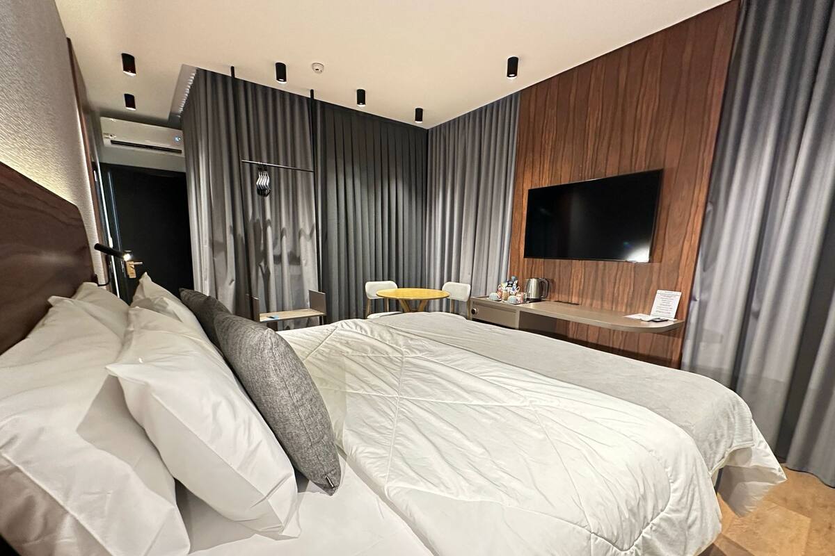 A modern hotel room with a large bed, a desk with a flat-screen TV, and a seating area with a table and chairs.