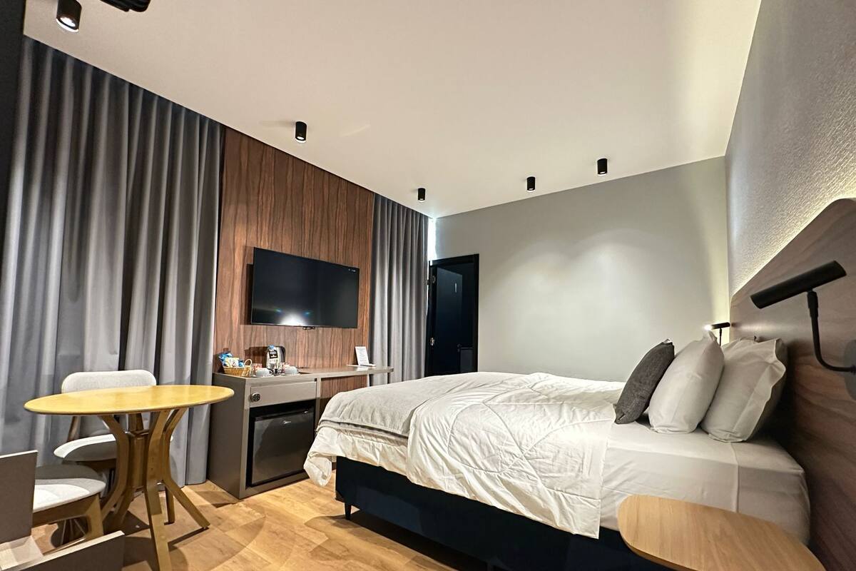 A hotel room with a bed, a desk, a chair, a TV, and a small table.