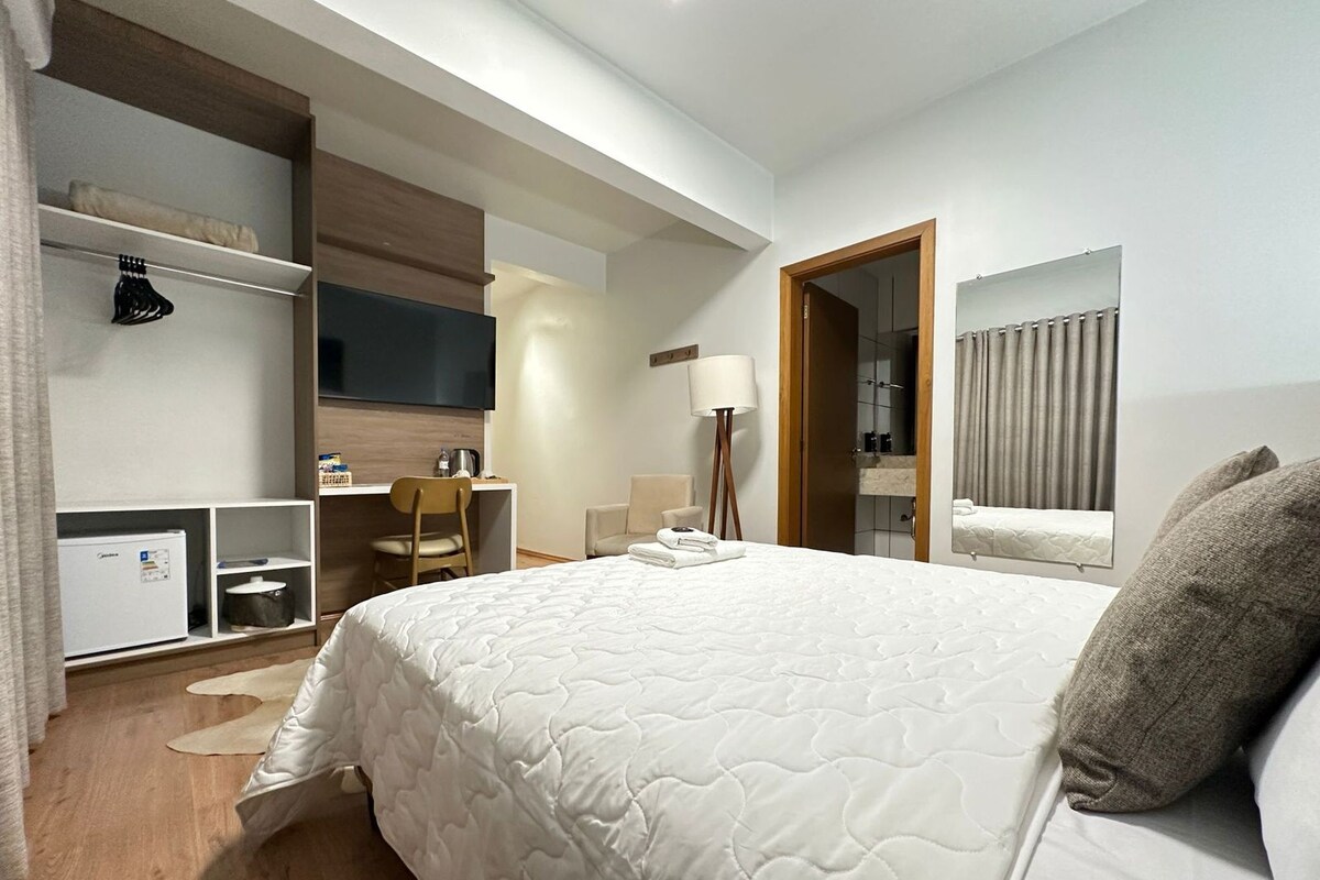 Una habitación de hotel con una cama grande, un escritorio, una silla, un televisor, un espejo y un armario.
