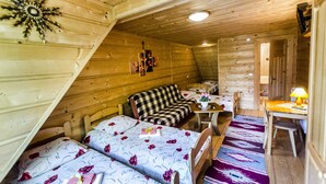 Una cabaña de madera acogedora con dos camas, un sofá, una mesa de comedor y una pequeña cocina.