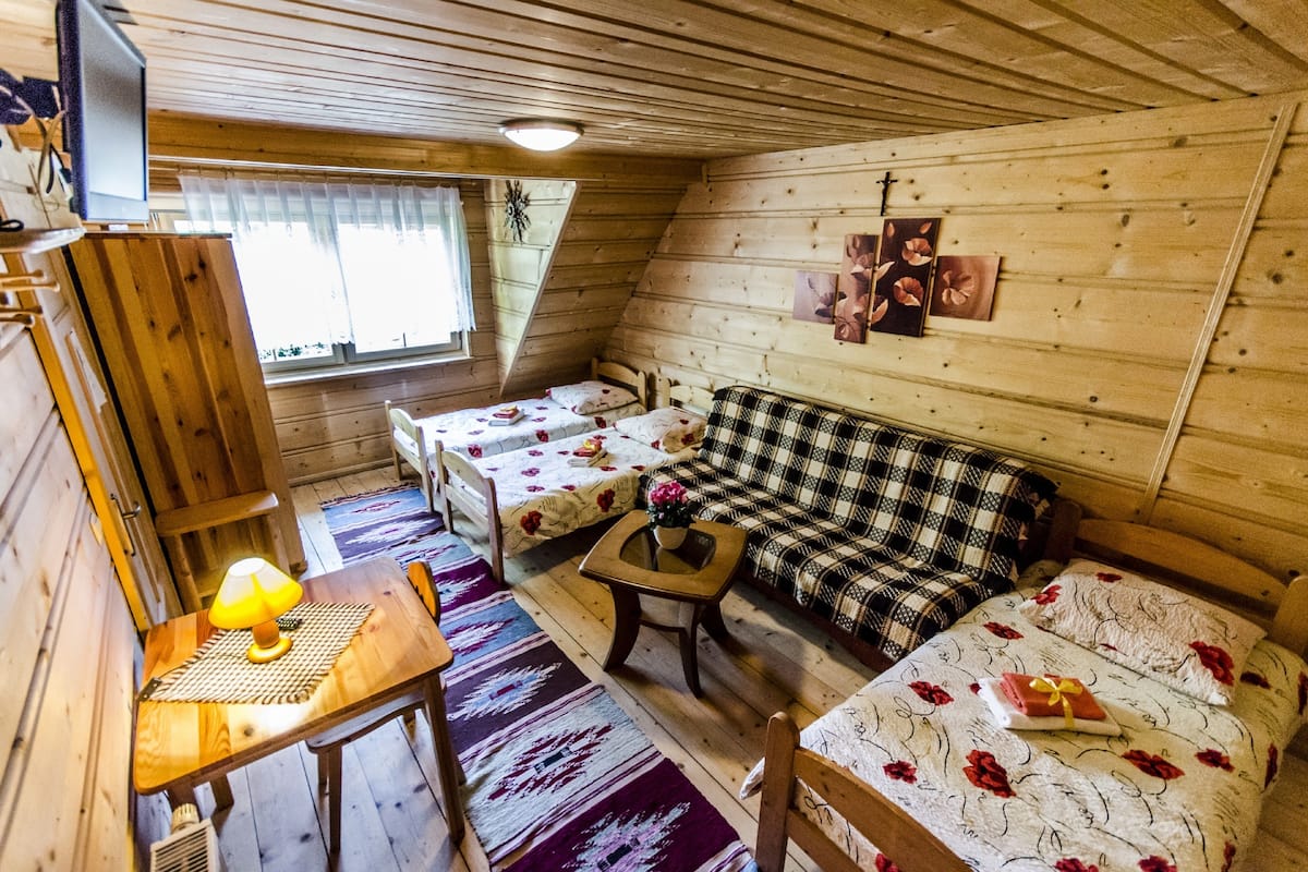 Una cabaña acogedora con dos camas individuales, un sofá, una mesita con lámpara y una ventana con cortinas.