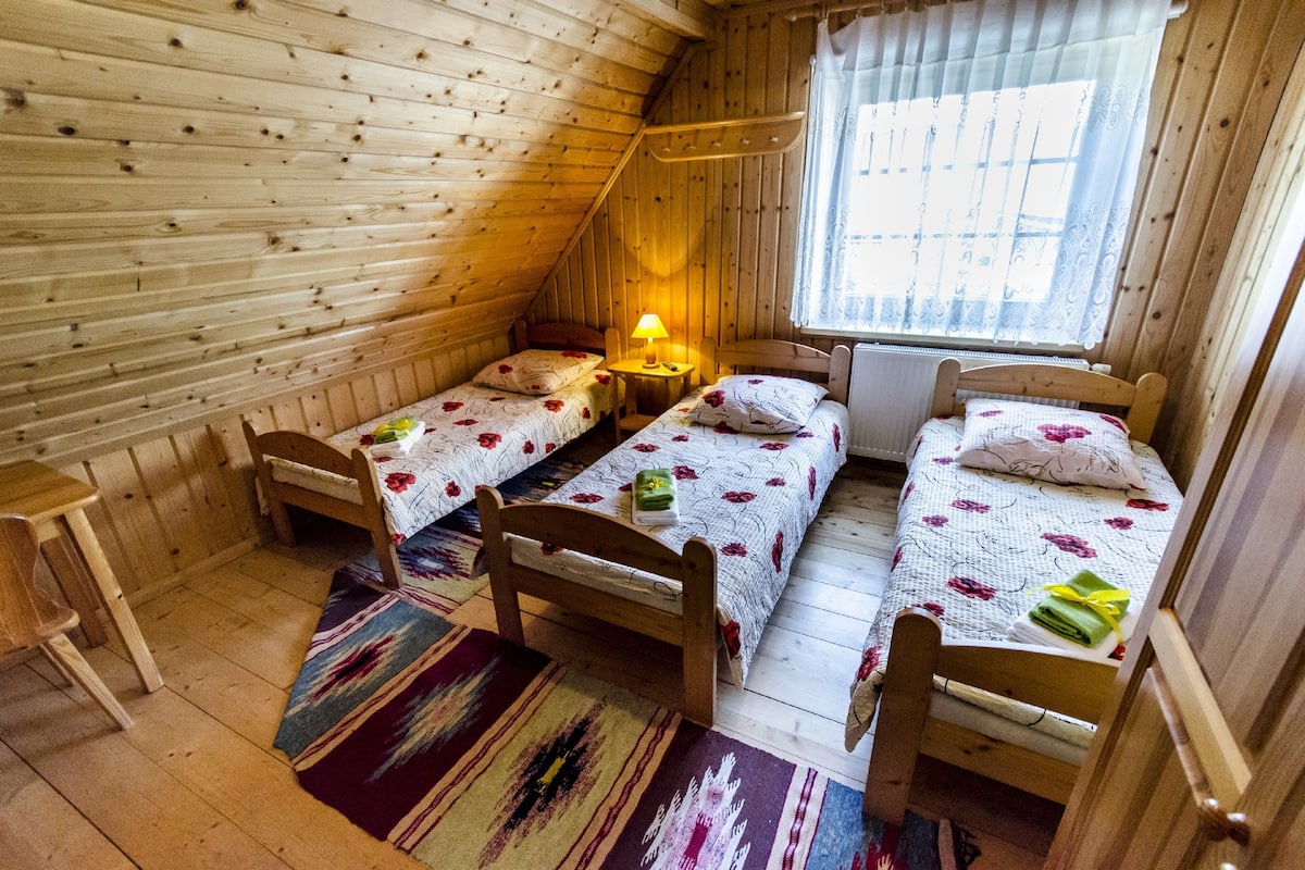 Un dormitorio acogedor en el ático con dos camas de madera, una mesita y una ventana con cortinas.