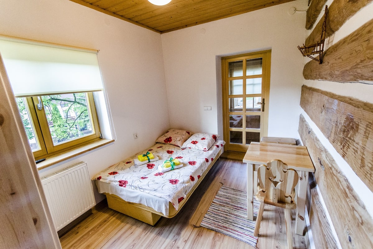 Una habitación pequeña y acogedora con una cama individual, un banco de madera y una ventana con vistas a la vegetación.