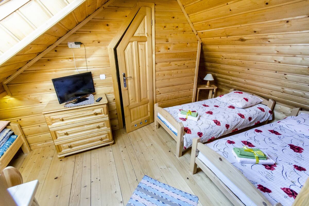 Una habitación acogedora tipo cabaña de madera con una cama, un escritorio con computadora, una lámpara y una ventana.