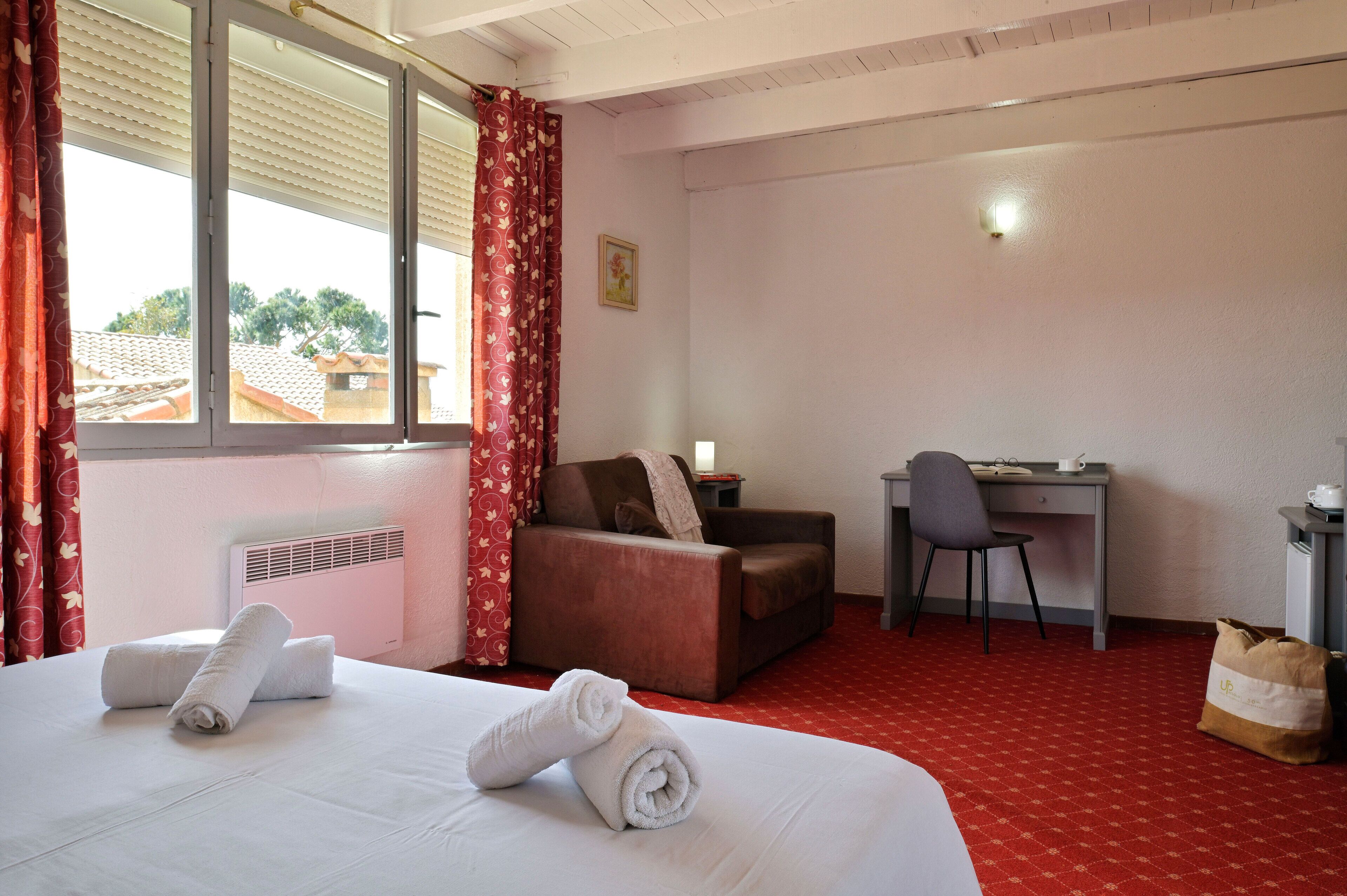 A hotel room with a bed, a desk, a chair, a sofa, and a window with curtains.