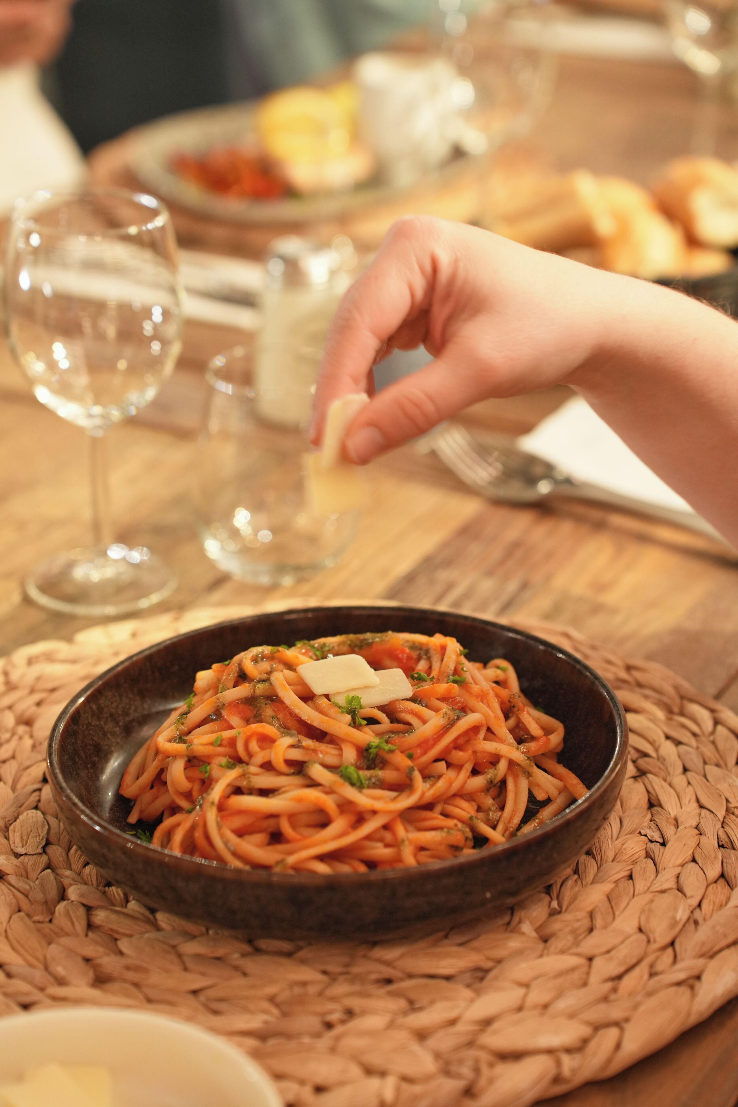 A bowl of spaghetti with a fork and a glass of water on a woven placemat.