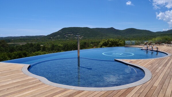 Relax by the serene infinity pool surrounded by lush green hills and a wooden deck.