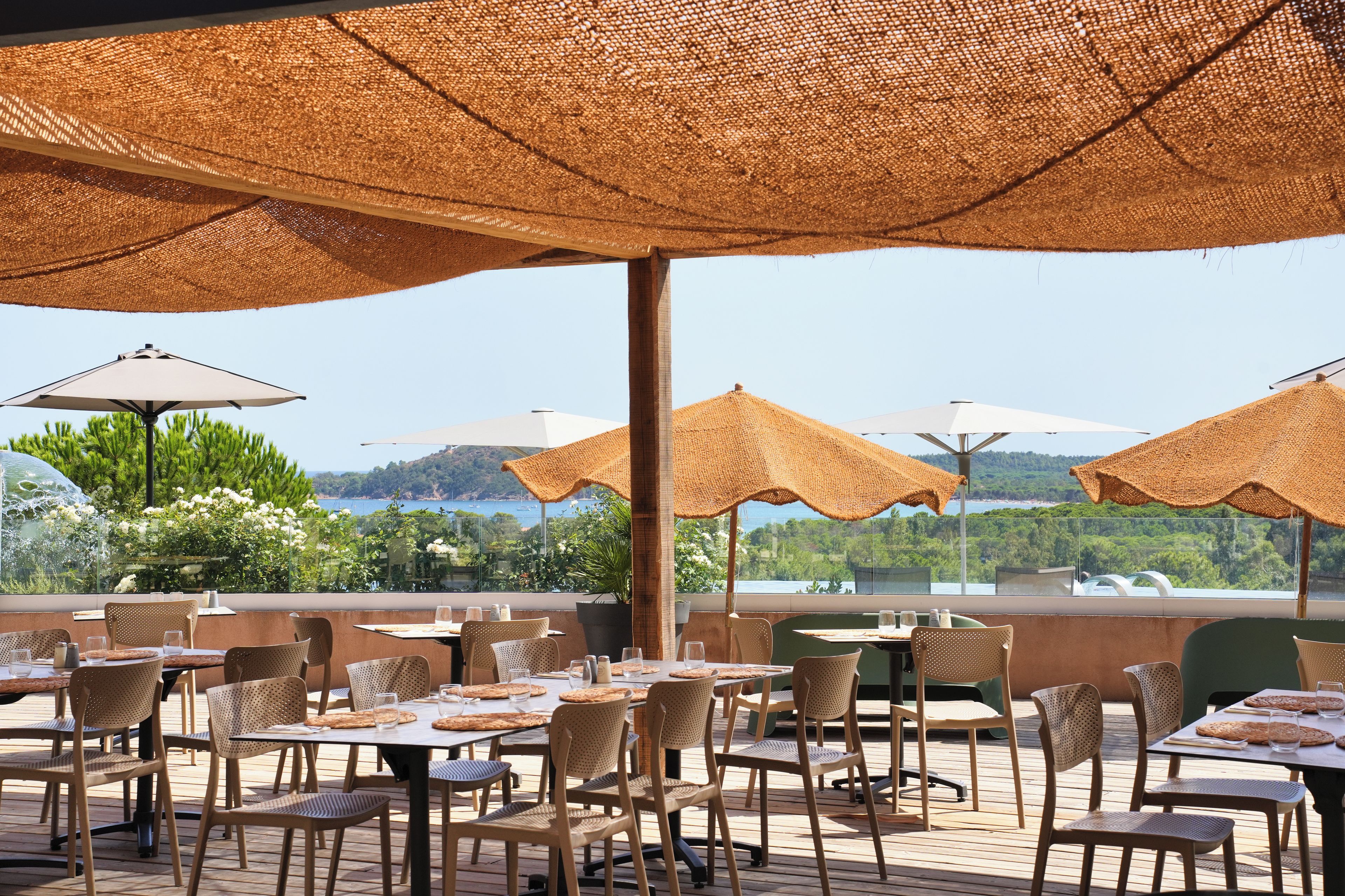 An outdoor dining area with tables and chairs, covered by woven umbrellas, overlooking a scenic landscape.
