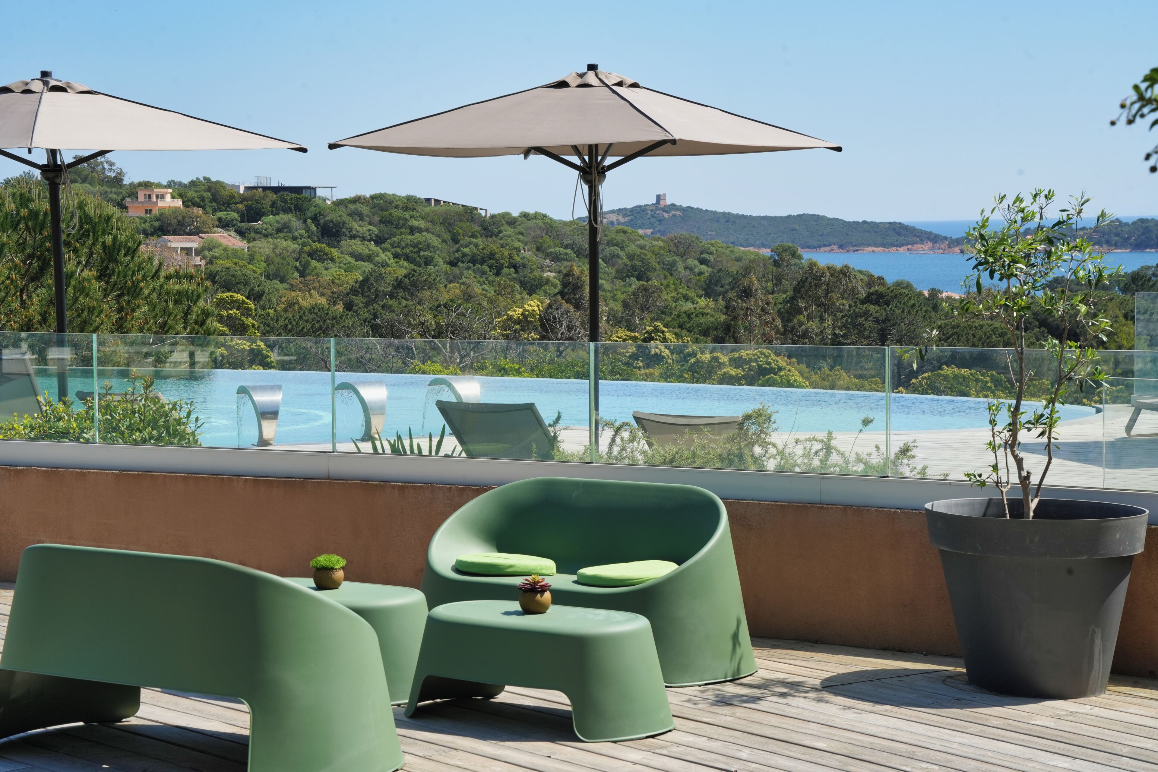 Une terrasse sur le toit avec une piscine, des chaises vertes et des parasols, offrant une vue panoramique sur un paysage magnifique.