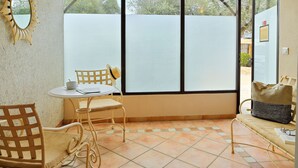 A room with a dining table, chairs, a bench, and a large window with a view of trees. - Hôtel U Paesolu (Zonza)