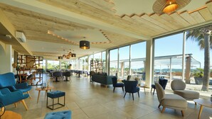 A spacious lobby with modern furniture, large windows, and a wooden ceiling. - Hôtel U Paesolu (Zonza)