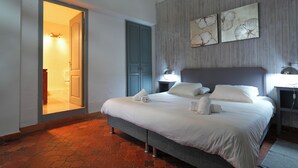 A hotel room with a bed, two wall-mounted lamps, a door leading to a bathroom, and two wall art pieces. - Hôtel U Paesolu (Zonza)
