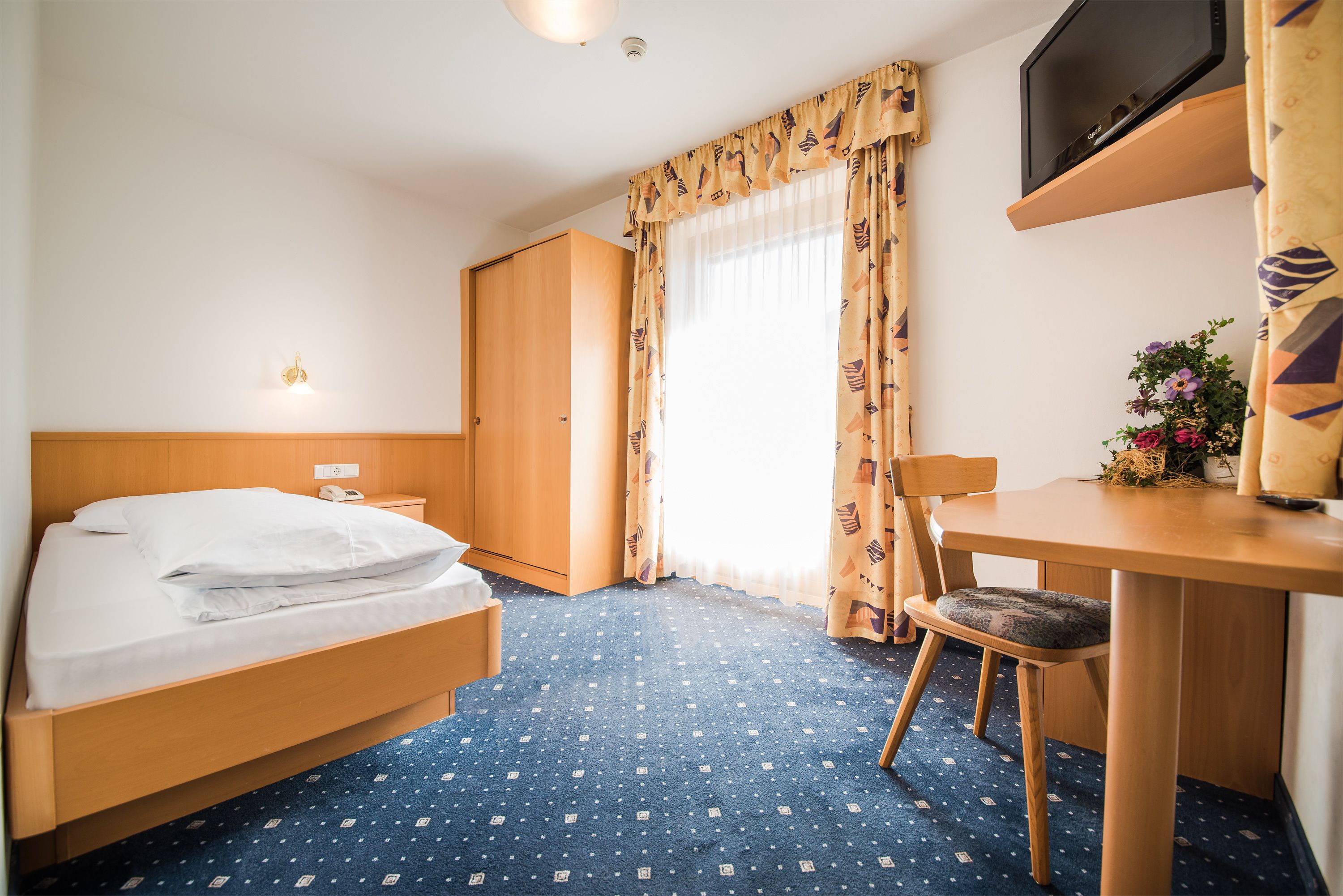 A hotel room with a bed, a desk, a chair, a TV, and a window with curtains.