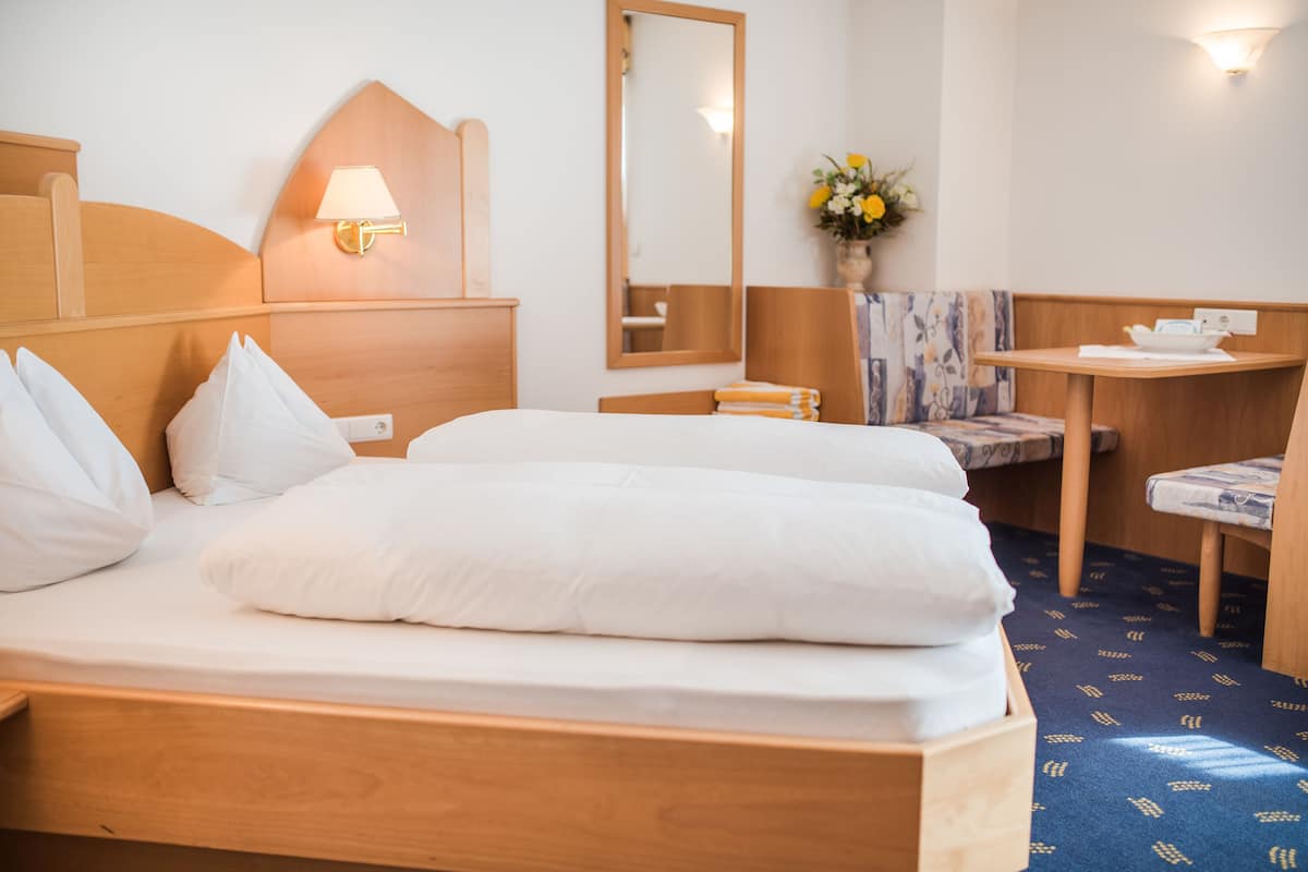 A hotel room with a wooden bed, a bedside table, a mirror, and a small desk with a chair.