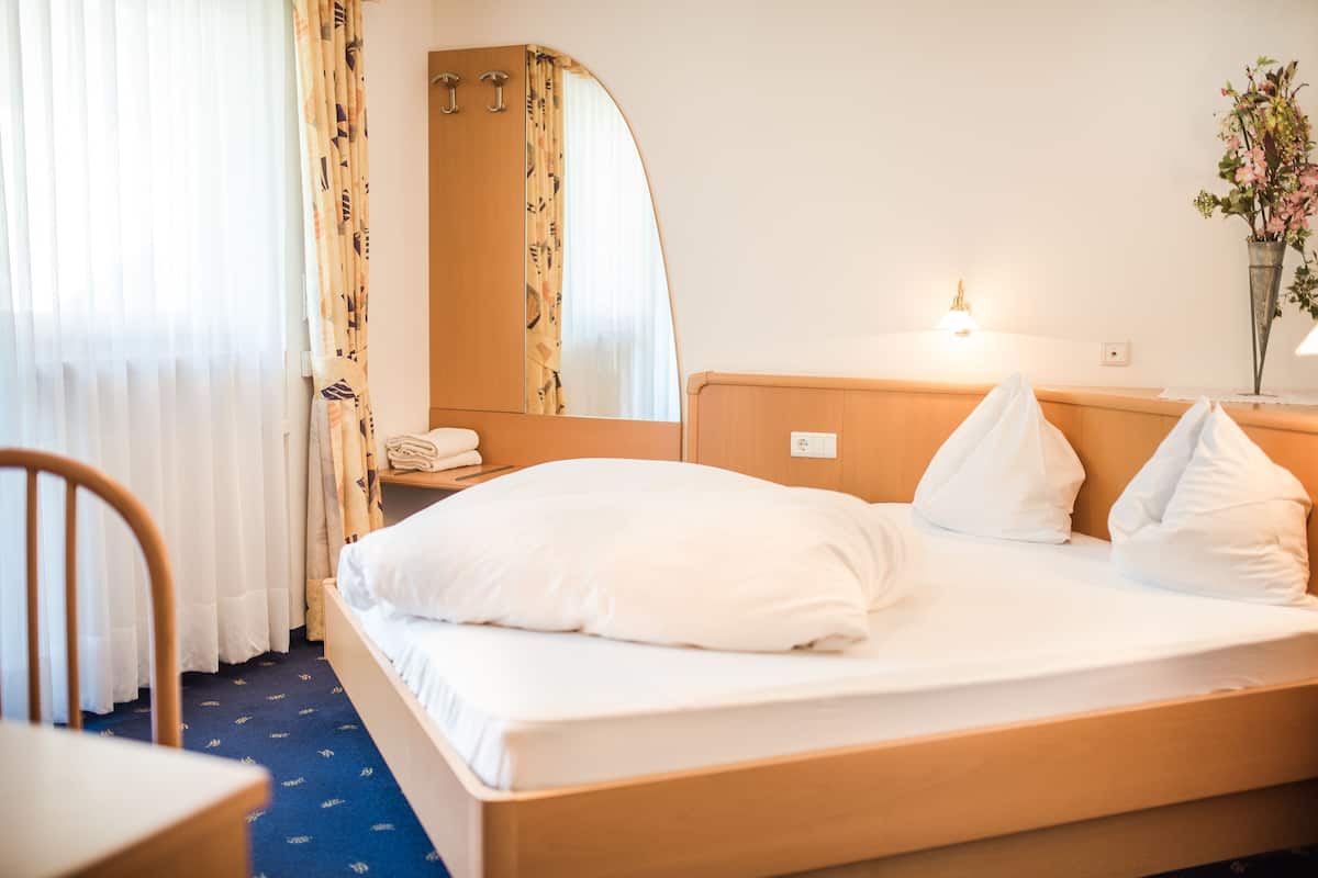 A hotel room with a bed, a chair, a mirror, a bedside table, and a lamp.
