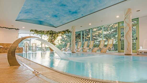 Una piscina interior con techo estrellado, ventanas amplias y sillones de descanso.