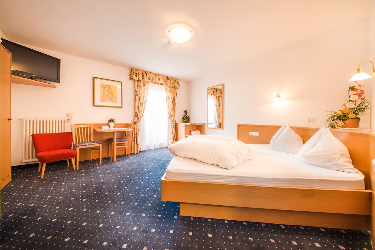 A hotel room with a bed, a desk, a chair, a TV, and a window with curtains.