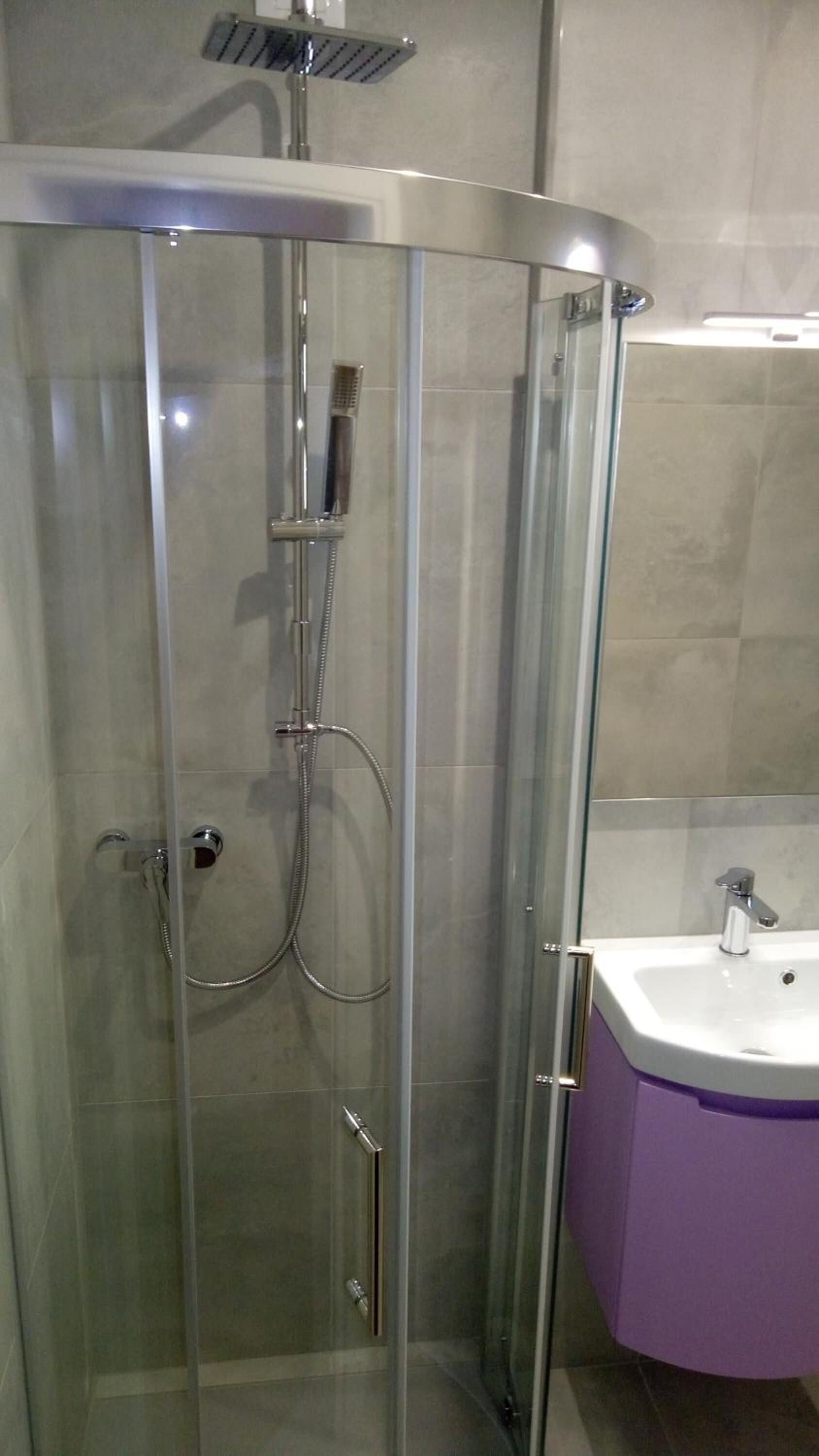 Cabina doccia in vetro con soffione a mano e rubinetto a parete.