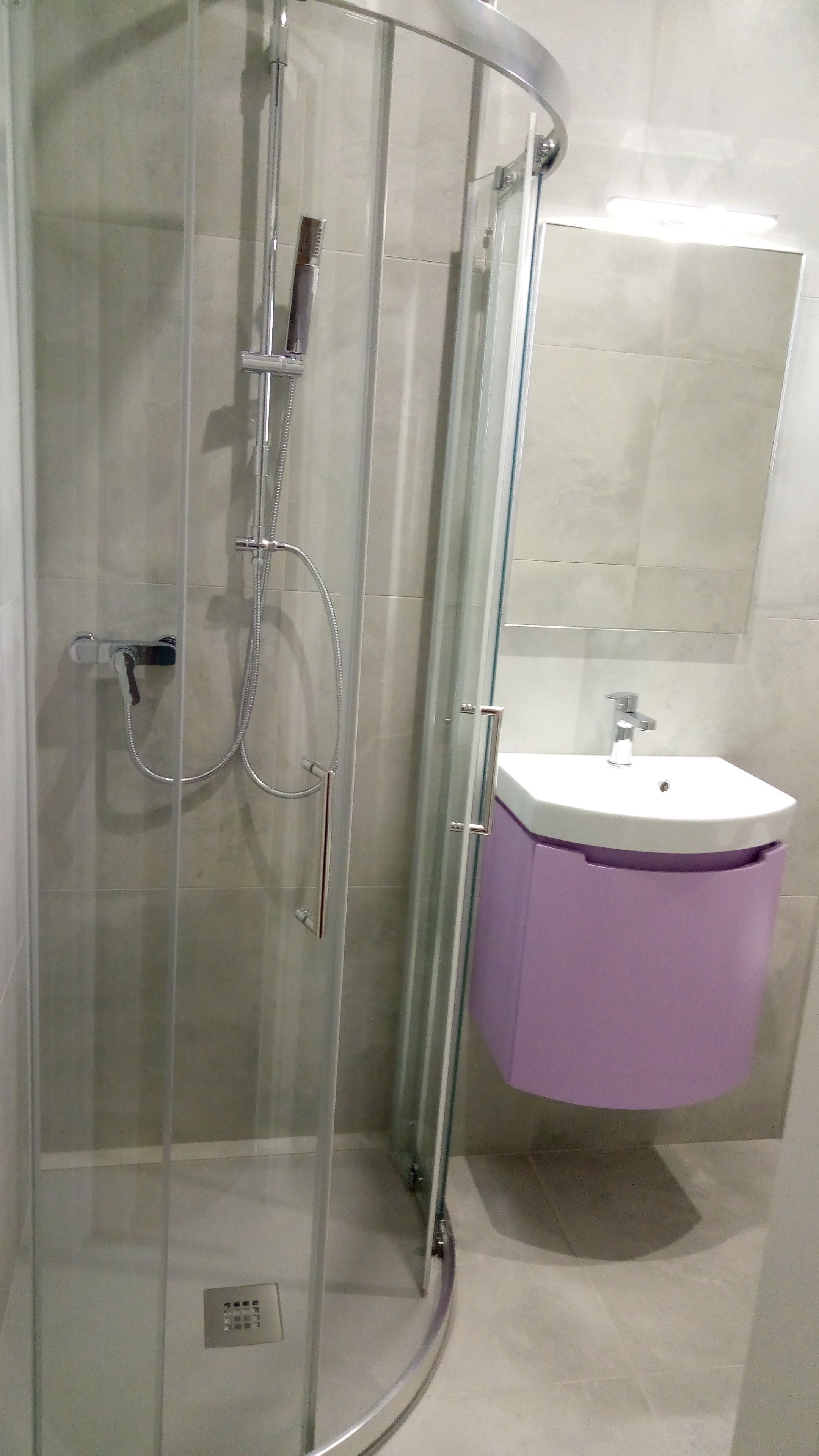 A glass-enclosed shower with a handheld showerhead and a wall-mounted faucet.
