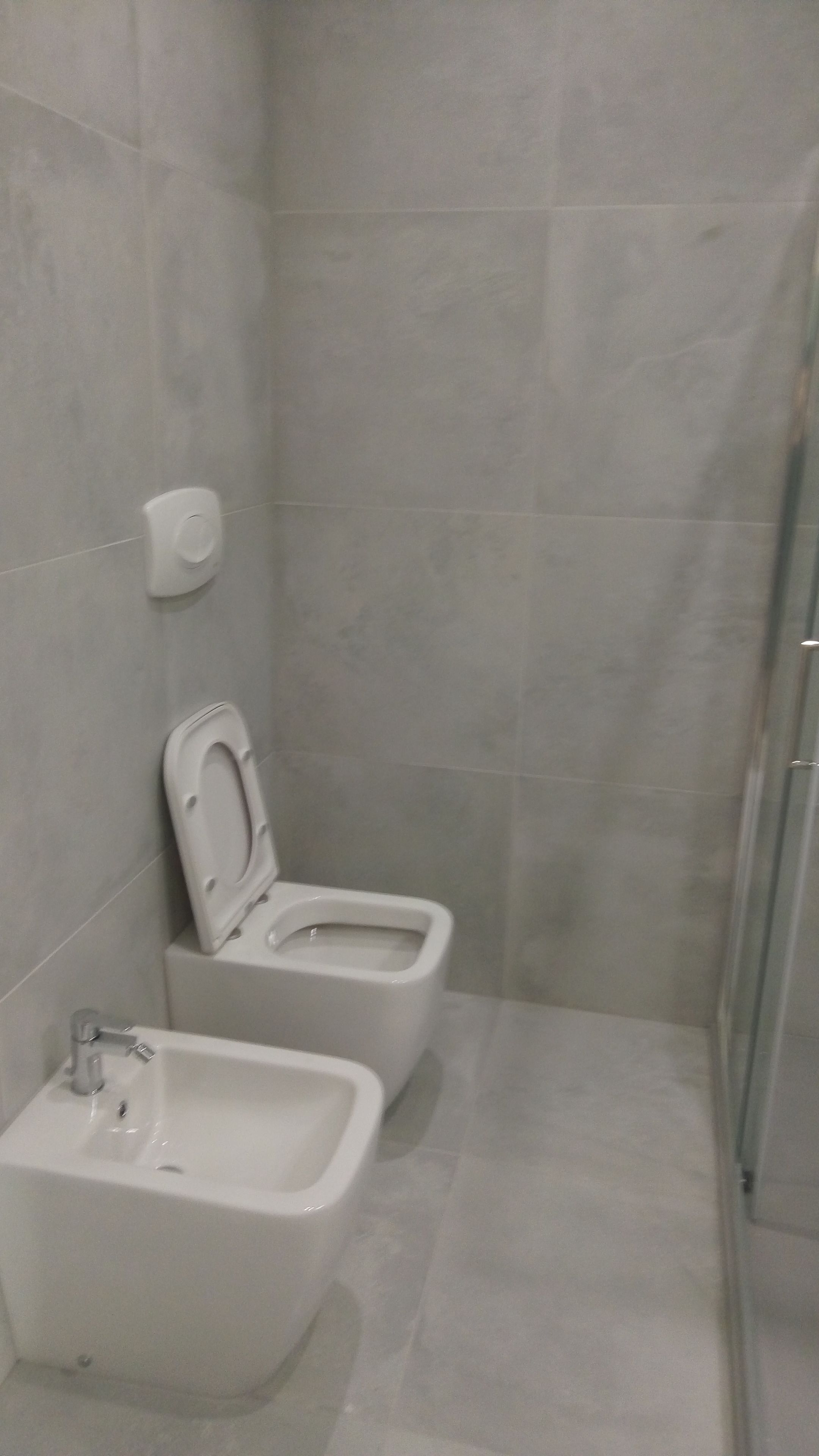 A small bathroom with two toilets, a sink, and a shower.