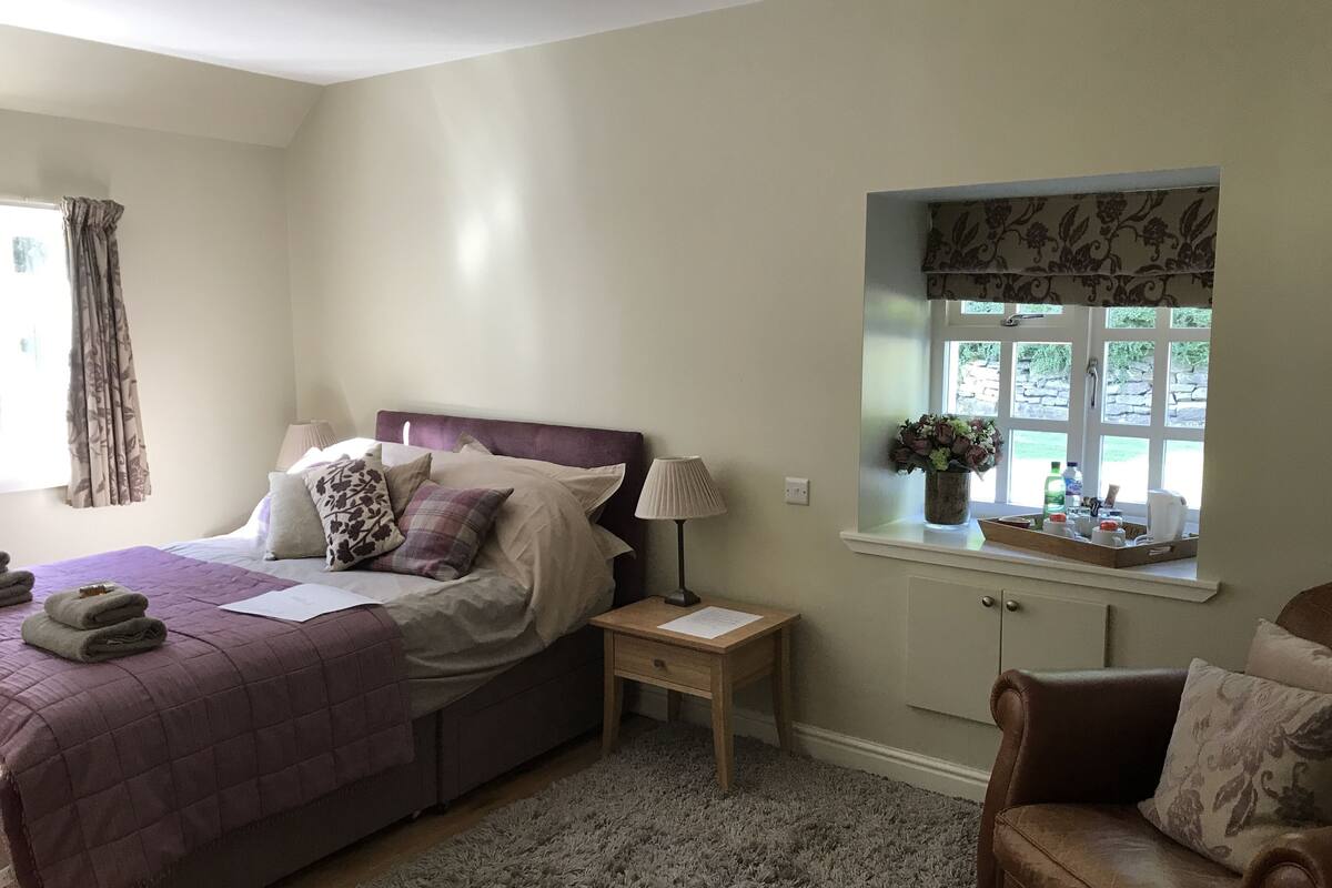 A bedroom with a bed, a nightstand, a window with a view, and a chair.