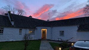 A white building with a stone roof, a paved entrance, and a car parked in front. - South Craighall Bed & Breakfast (Glasgow)