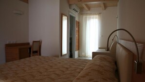 A bedroom with a large bed, a desk, and a chair. There is a window with curtains and a door leading to another room. - Agritur Ponte Alto (Trento)
