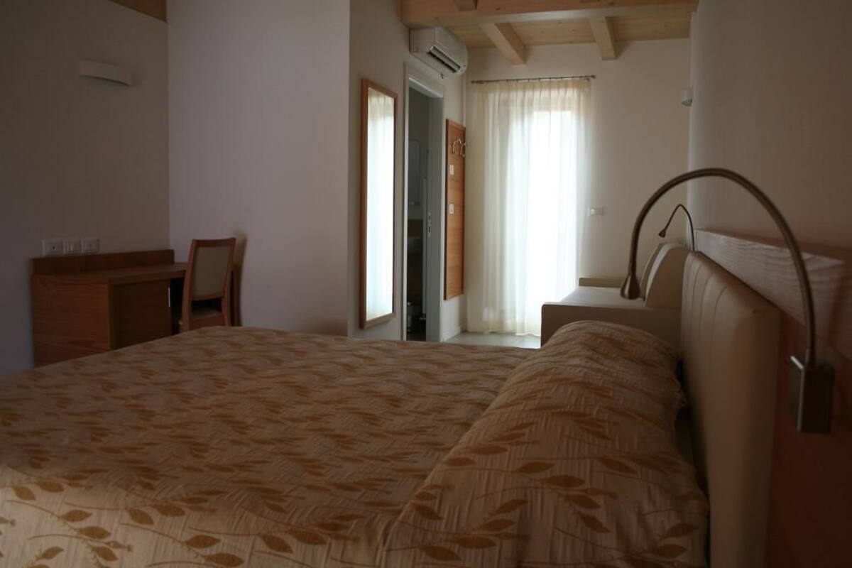 A bedroom with a large bed, a desk, and a chair. There is a window with curtains and a door leading to another room.