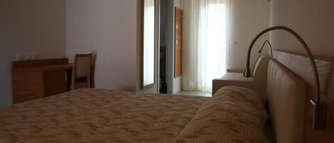 A bedroom with a large bed, a desk, and a chair. There is a window with curtains and a door leading to another room.