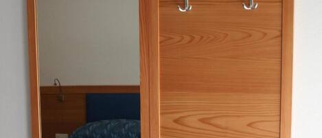 A wooden wardrobe with two silver handles and a mirror.
