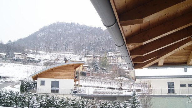 A modern building with a wooden facade and a sloped roof, set against a snowy hillside with residential buildings in the background. - Agritur Ponte Alto (Trento)