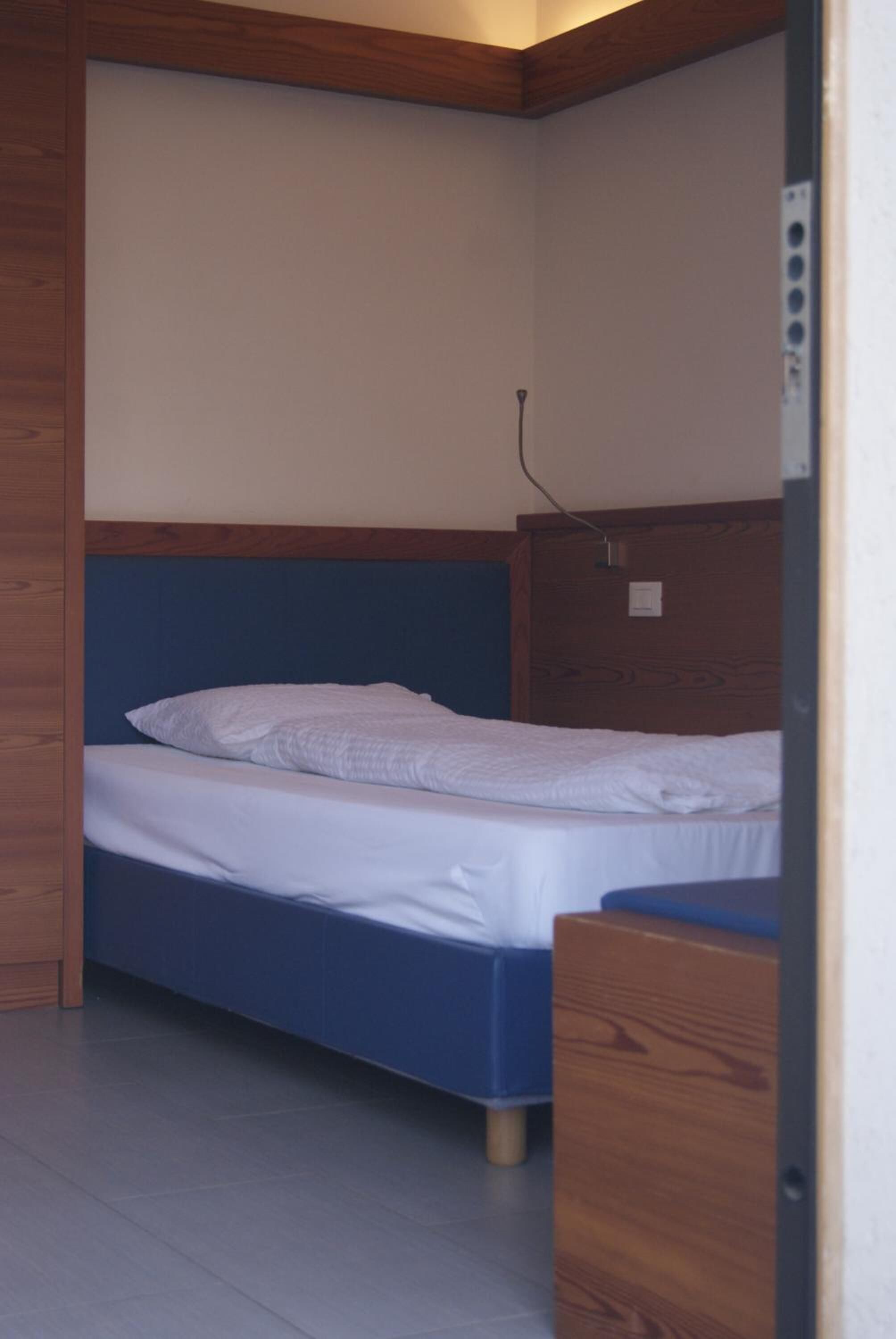 Une petite pièce, de taille modeste, comprenant un lit simple, une tête de lit en bois et un petit bureau en bois.