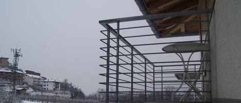 Un balcón con barandilla de metal que da a un paisaje nevado y edificios al fondo.