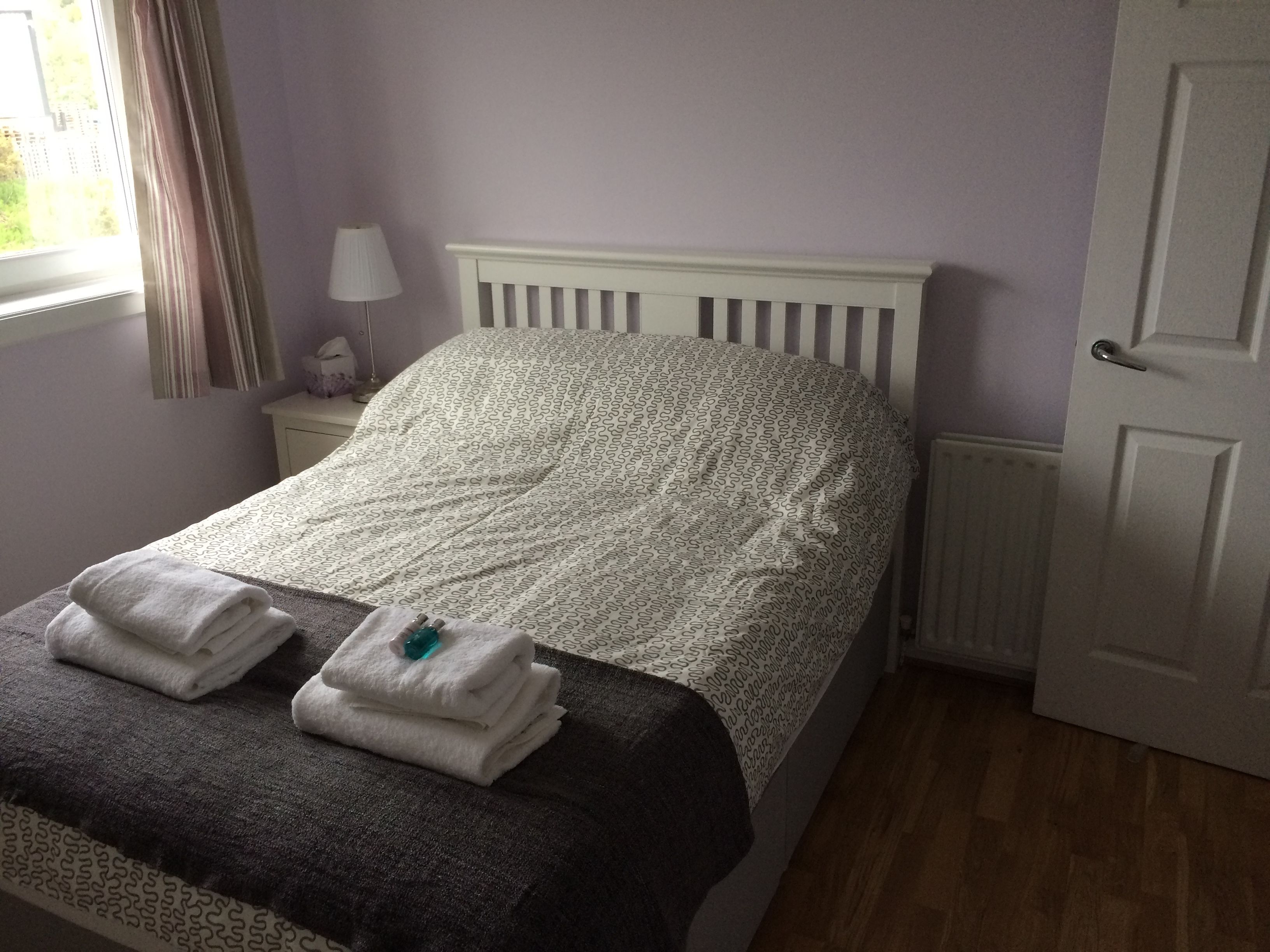 A neatly made bed with a patterned duvet, a bedside lamp, and a window with curtains.