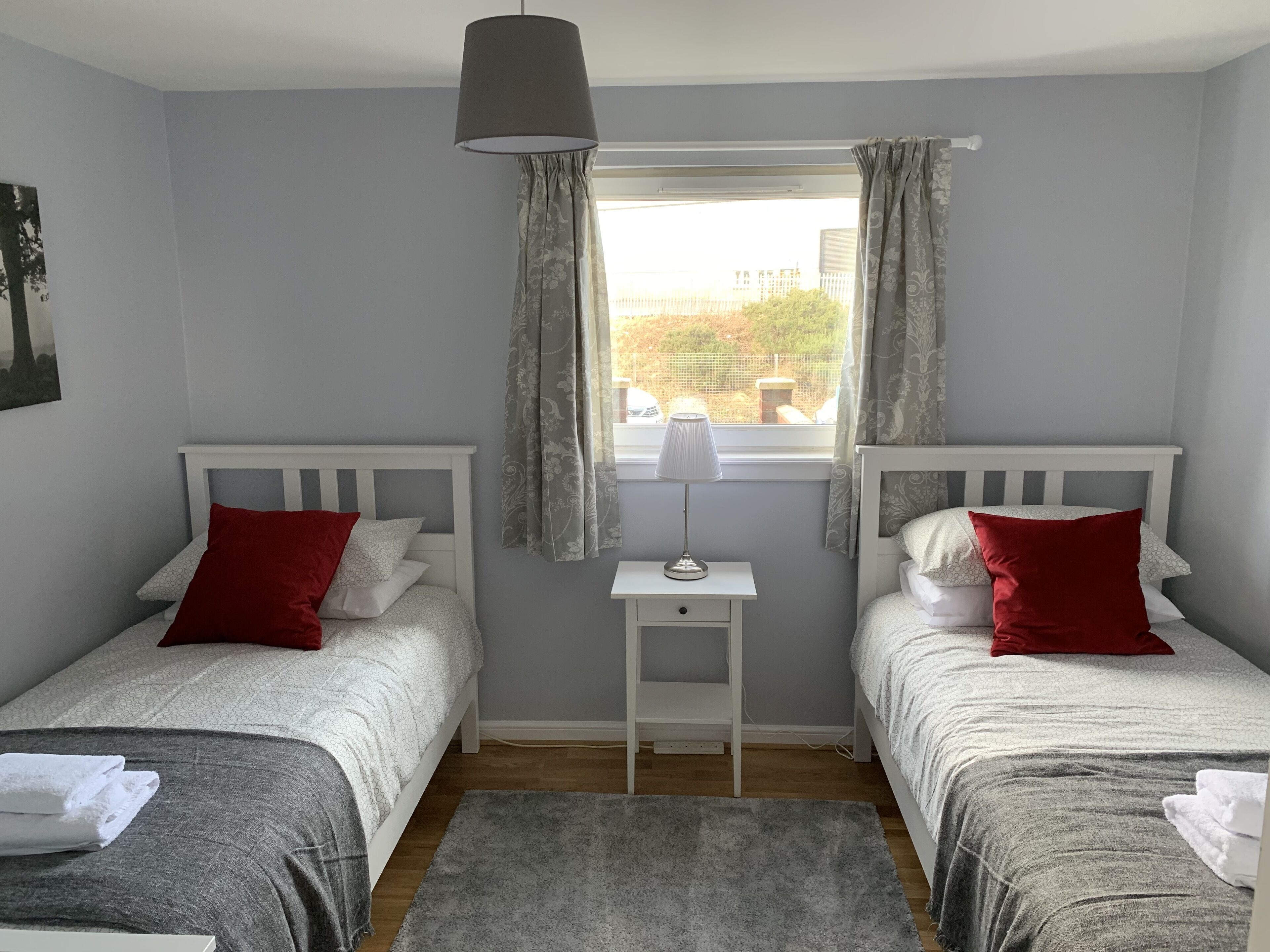 Een slaapkamer met twee bedden, een klein tafeltje, een lamp en een raam met gordijnen.