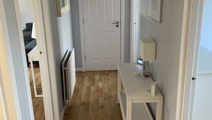 A hallway with a white door, a desk with a lamp, and a framed picture on the wall. - Serviced Apartments East Kilbride (Glasgow)
