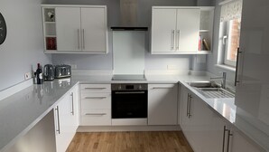A modern kitchen with white cabinets, a Bosch dishwasher, a built-in oven, and a window with patterned curtains. - Serviced Apartments East Kilbride (Glasgow)
