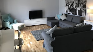 A modern living room with a flat-screen TV, grey sofas, a white entertainment unit, and a cityscape wall art. - Serviced Apartments East Kilbride (Glasgow)