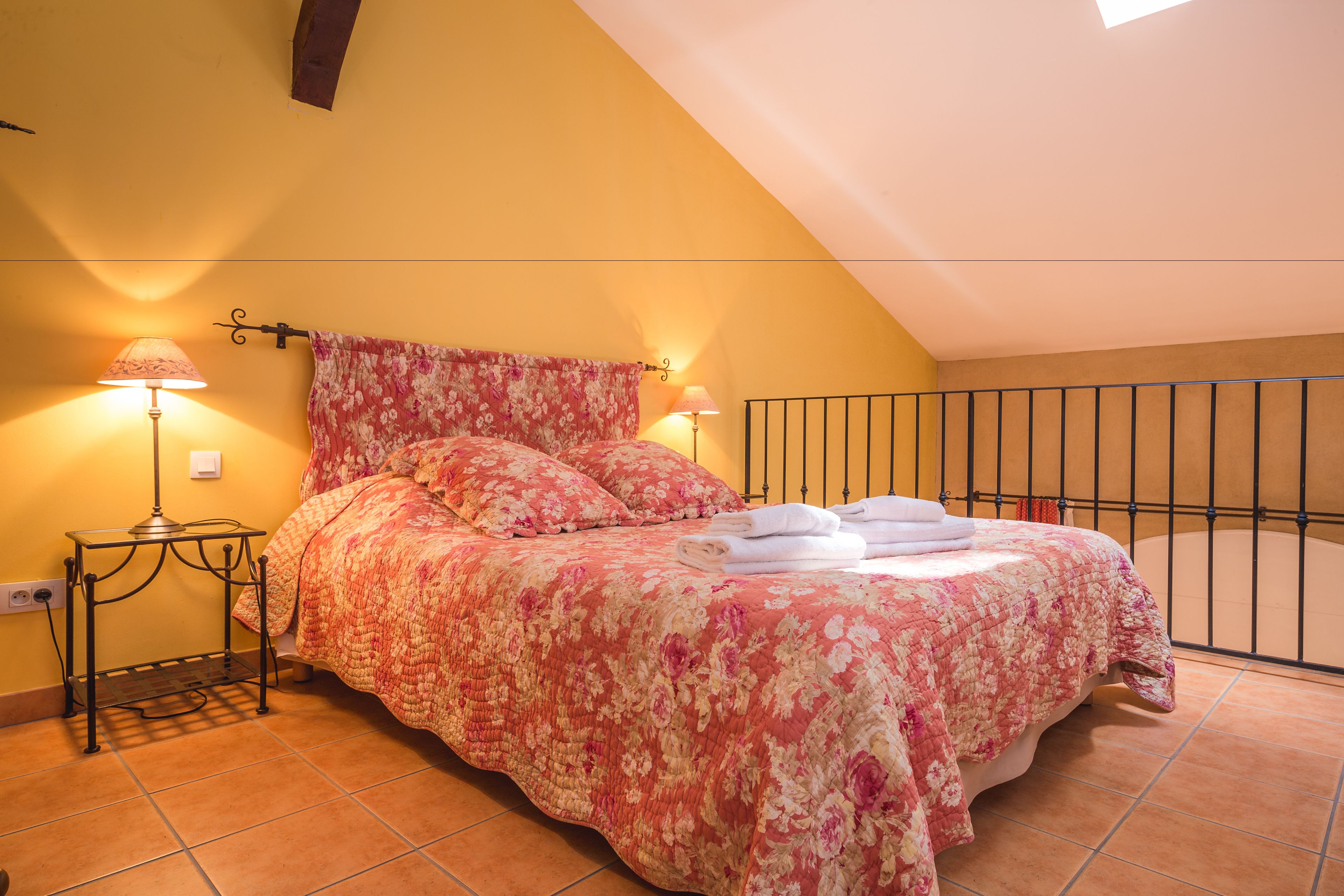 A bedroom with a bed, a nightstand, a lamp, and a window with a view of the outside.